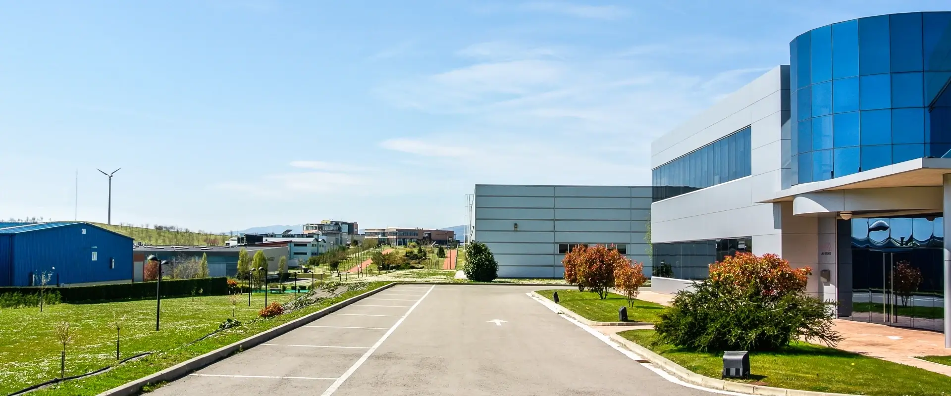 Vista exterior de un parque industrial con edificios modernos, fachadas de vidrio y metal, rodeado de áreas verdes bien cuidadas